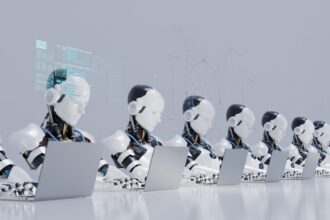 Row of humanoid robot coworkers working at desks with laptops, illustrating persistent AI agents