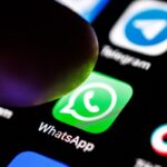 iPhone showing the WhatsApp app icon on a wooden desk