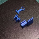 3D printed replacement clip designs resting on a printer build plate after testing AI-generated models